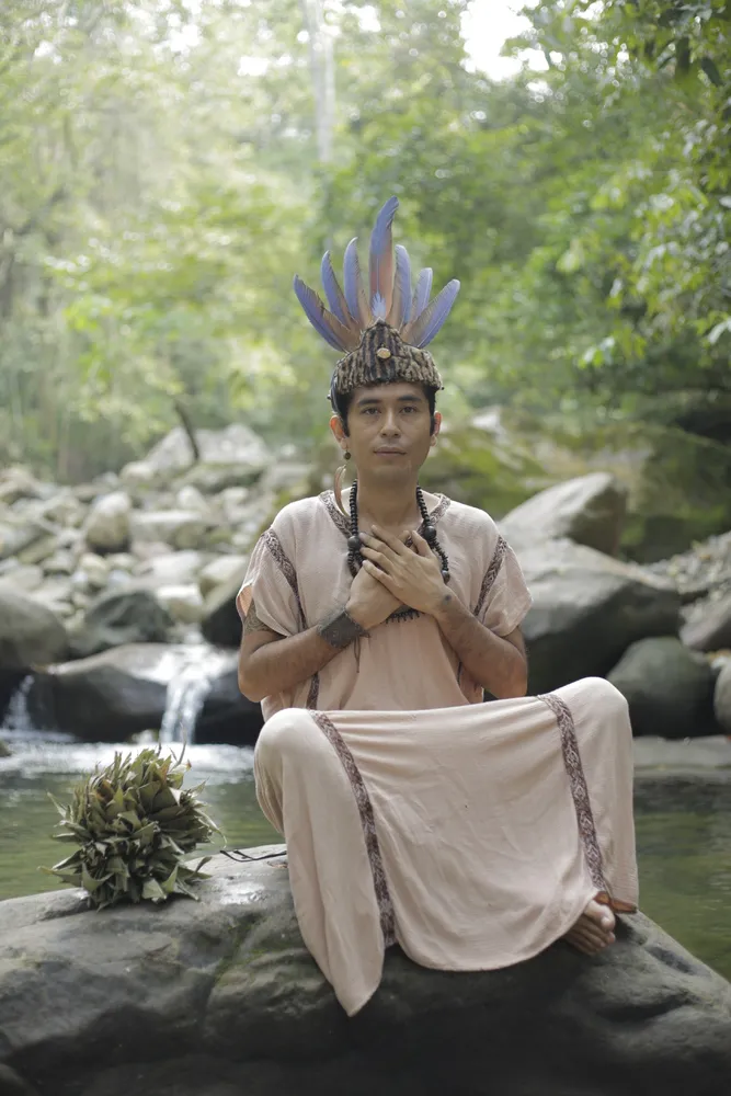 Maestro Qinty in ceremonial dress, hands over heart by the river